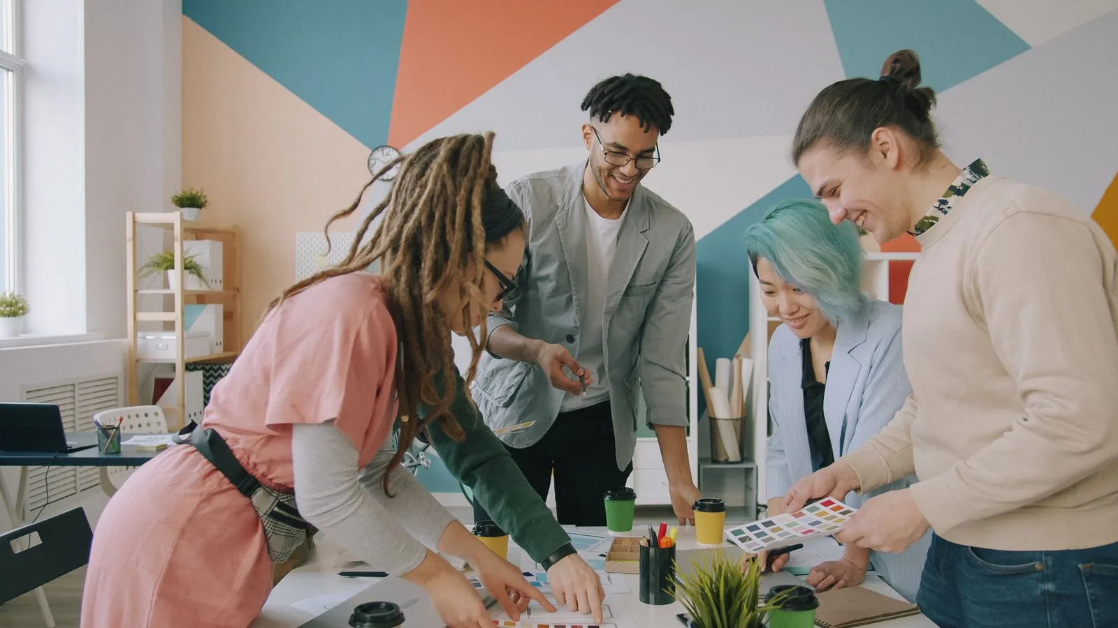 Equipe reunida em volta de uma mesa planejando um projeto, em um escritório com parede colorida