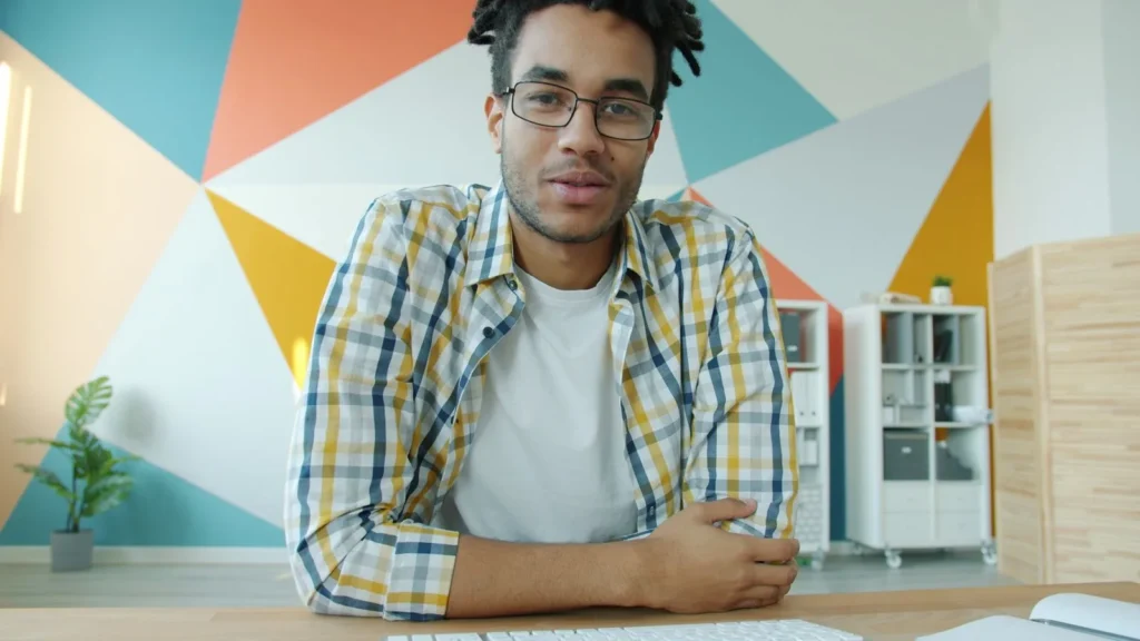 Homem sorrindo em frente a uma parede com formas geométricas coloridas, como em uma chamada de vídeo