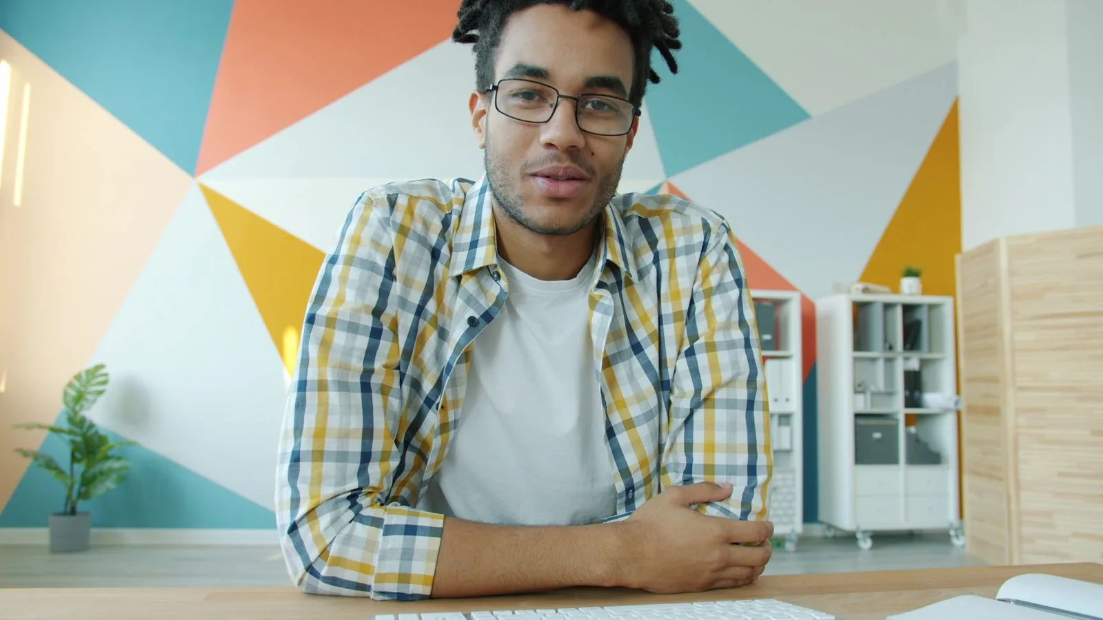Homem sorrindo em frente a uma parede com formas geométricas coloridas, como em uma chamada de vídeo